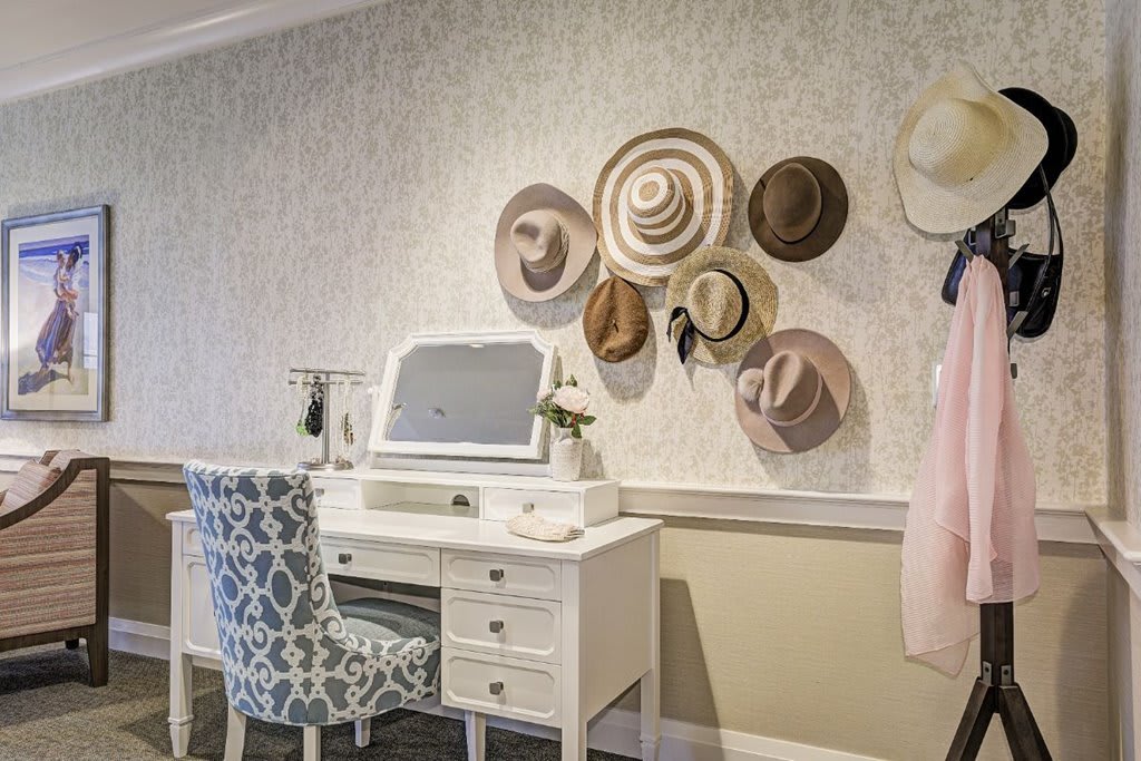 A cozy vanity setup with a white desk and patterned chair, adorned with hats on the wall.