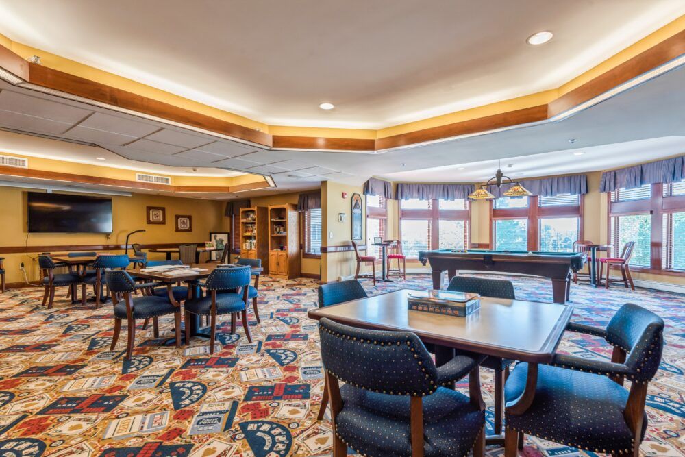 A spacious and well-lit lounge area featuring tables, chairs, and a pool table on a colorful carpet.