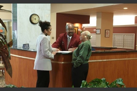Three people having a conversation at a reception desk in an office setting.
