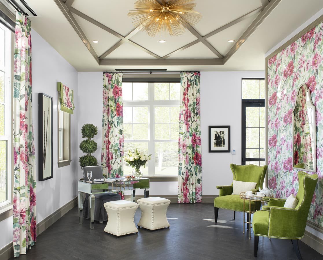 A stylish living room featuring floral curtains and green chairs, complemented by modern decor and ample natural light.