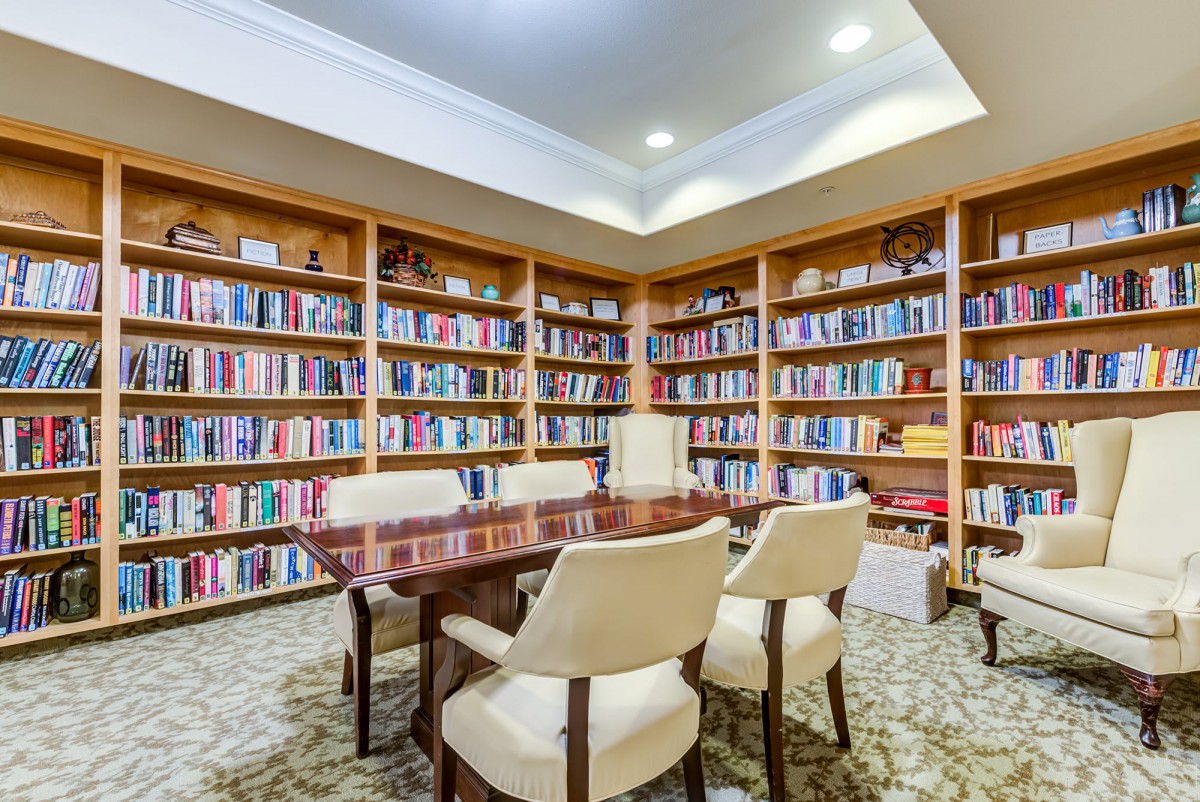 A cozy library with wooden bookshelves filled with books, surrounding a table and chairs.