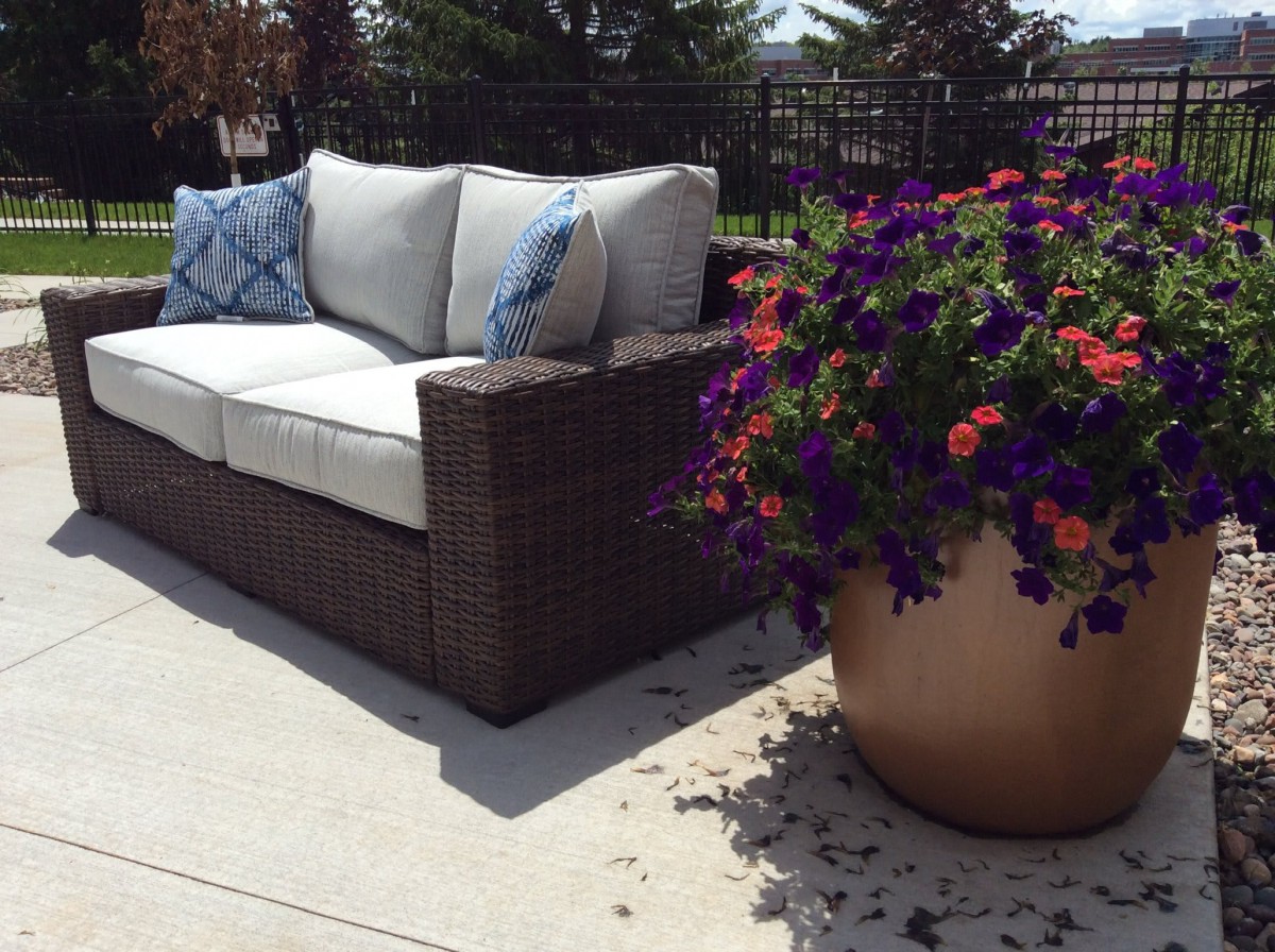 A comfortable patio sofa with cushions next to a vibrant potted flower arrangement on a sunny terrace.