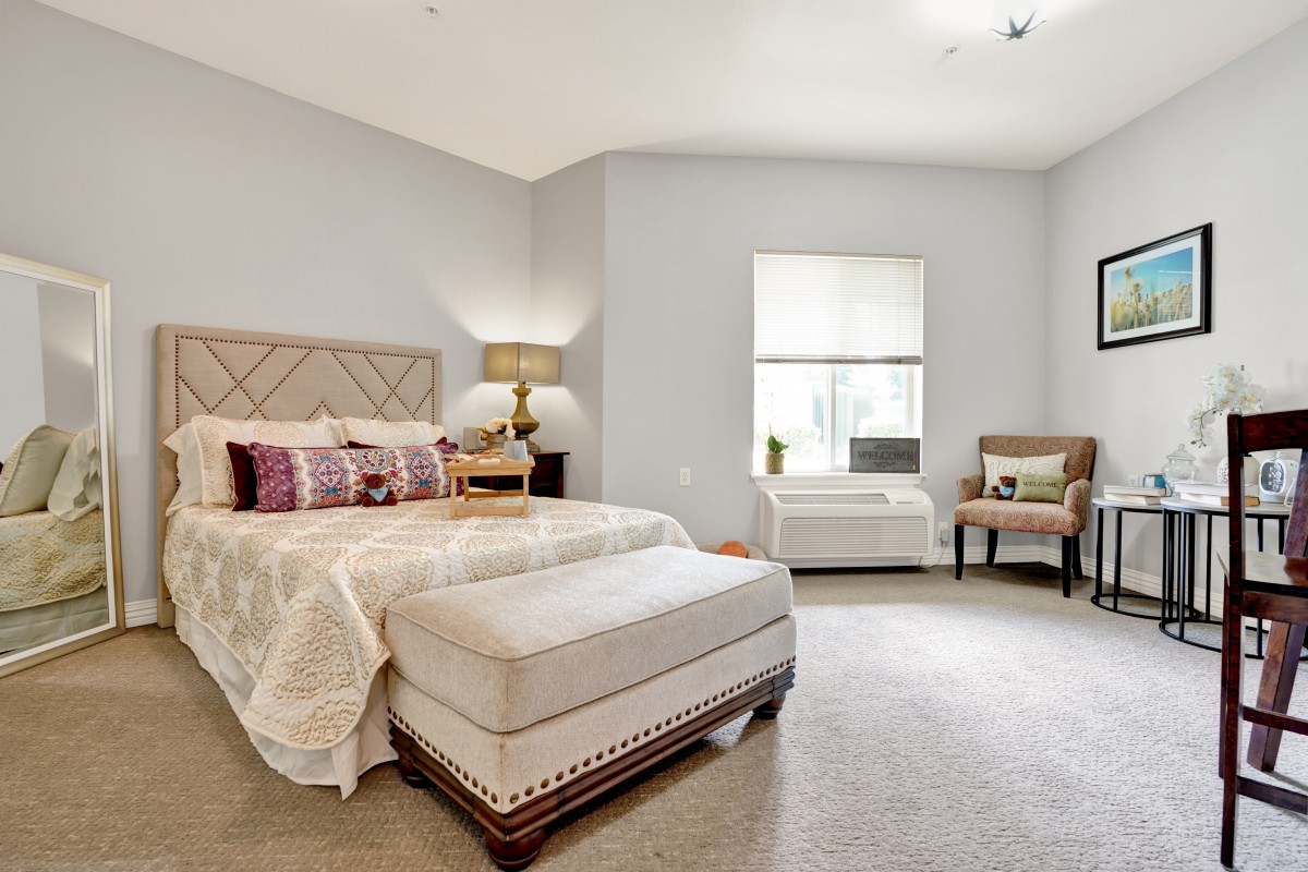 A bright and modern bedroom with elegant decor, featuring a bed, armchair, and window allowing natural light.