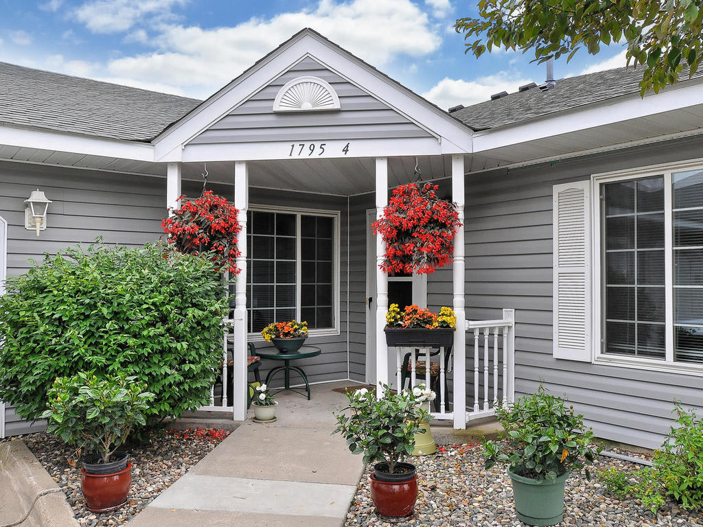 A charming house entrance with gray siding, featuring a welcoming front porch adorned with hanging and potted plants.