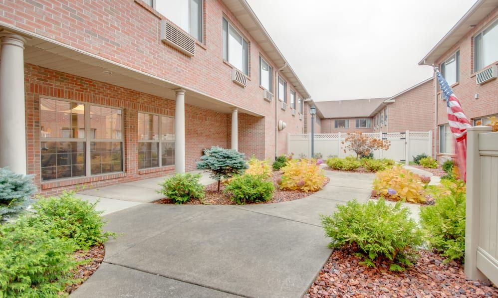 A view of a courtyard with landscaping, featuring shrubs and a concrete sidewalk in front of a brick building.