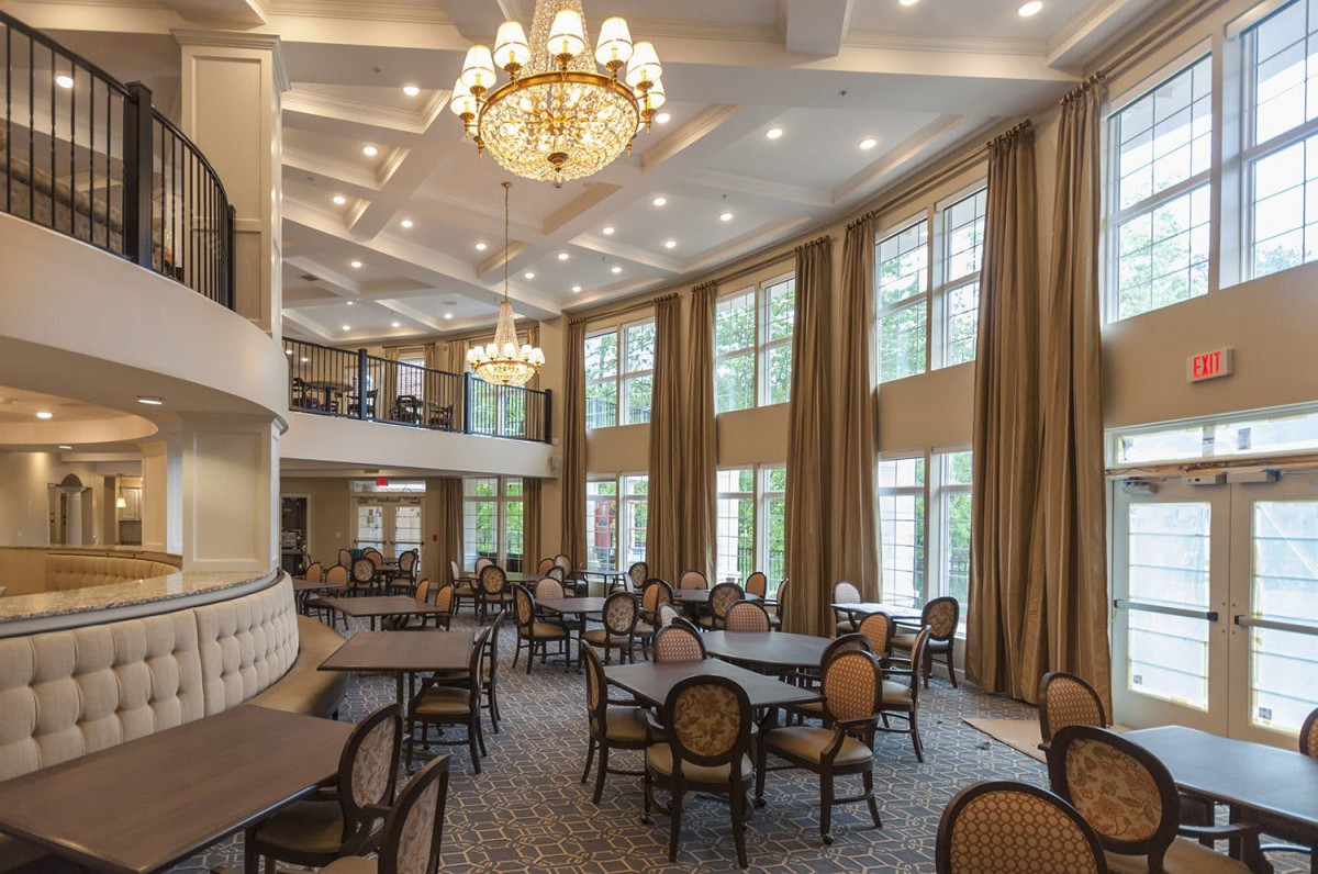 A spacious dining area with elegant chandeliers, large windows, and neatly arranged tables and chairs.