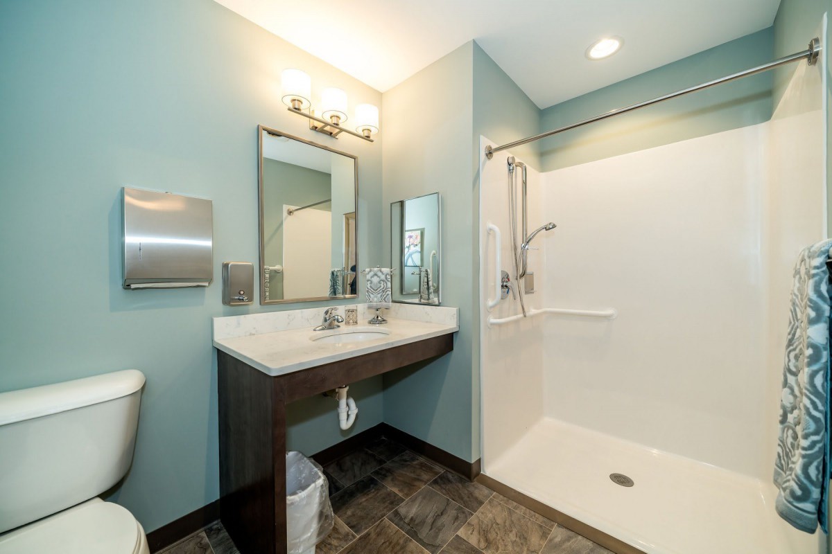 A modern and accessible bathroom featuring a spacious shower, sink with mirrors, and bright lighting.
