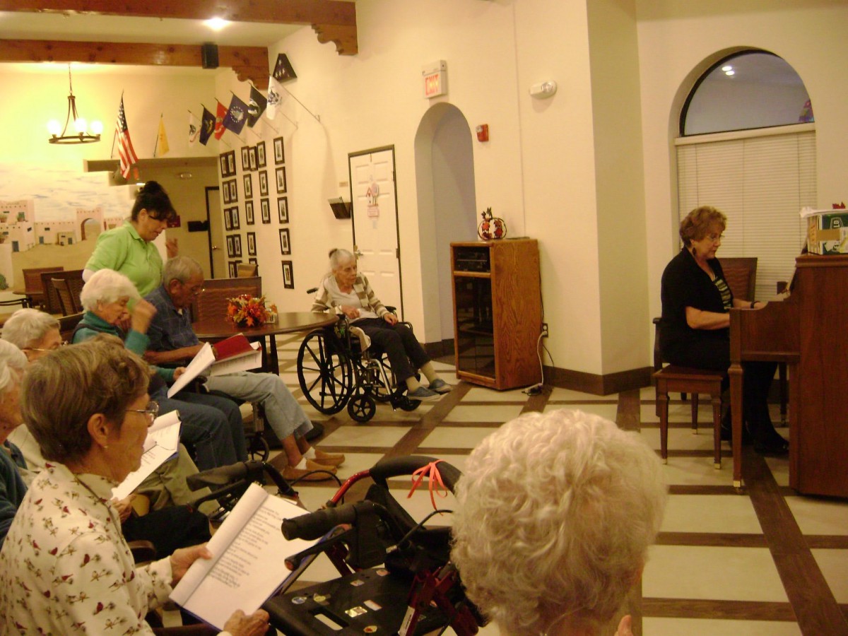 A group of seniors gathered in a communal area, some in wheelchairs, engaging in an activity.