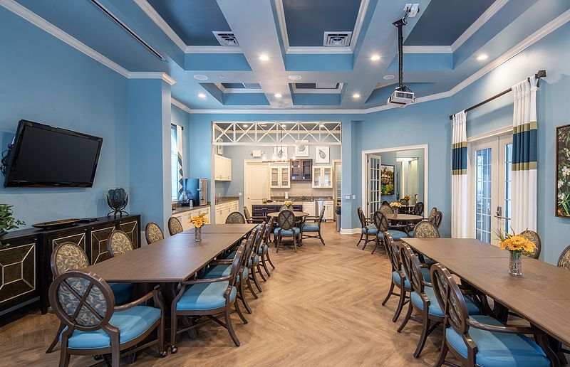 A spacious dining room with blue walls, elegantly arranged tables and chairs, featuring a modern ceiling design and wooden flooring.