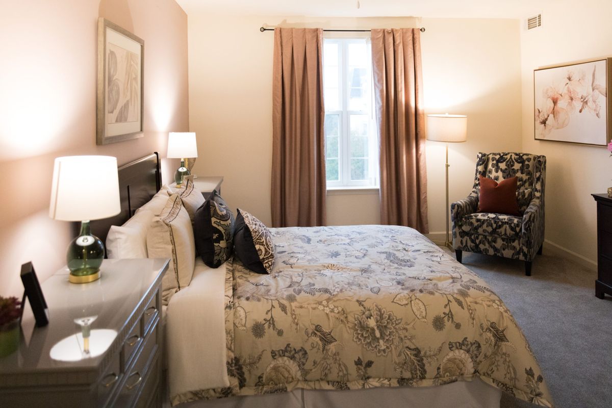 A cozy bedroom with elegant decor, featuring a comfortable bed, bedside lamps, and a patterned armchair.
