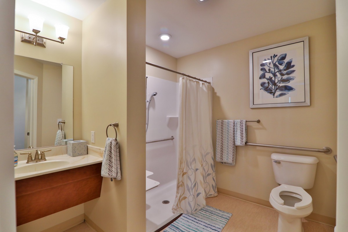 A neatly arranged bathroom featuring a shower with a curtain, sink, toilet, and decorative artwork on the wall.