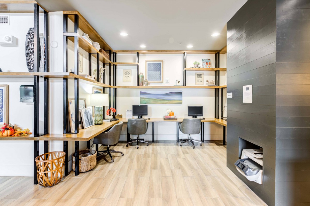 A modern office workspace featuring multiple desks, computers, and shelving.