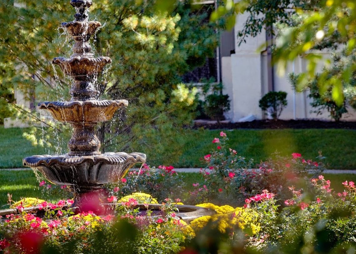 A beautiful garden with a multi-tiered fountain surrounded by vibrant flowers.