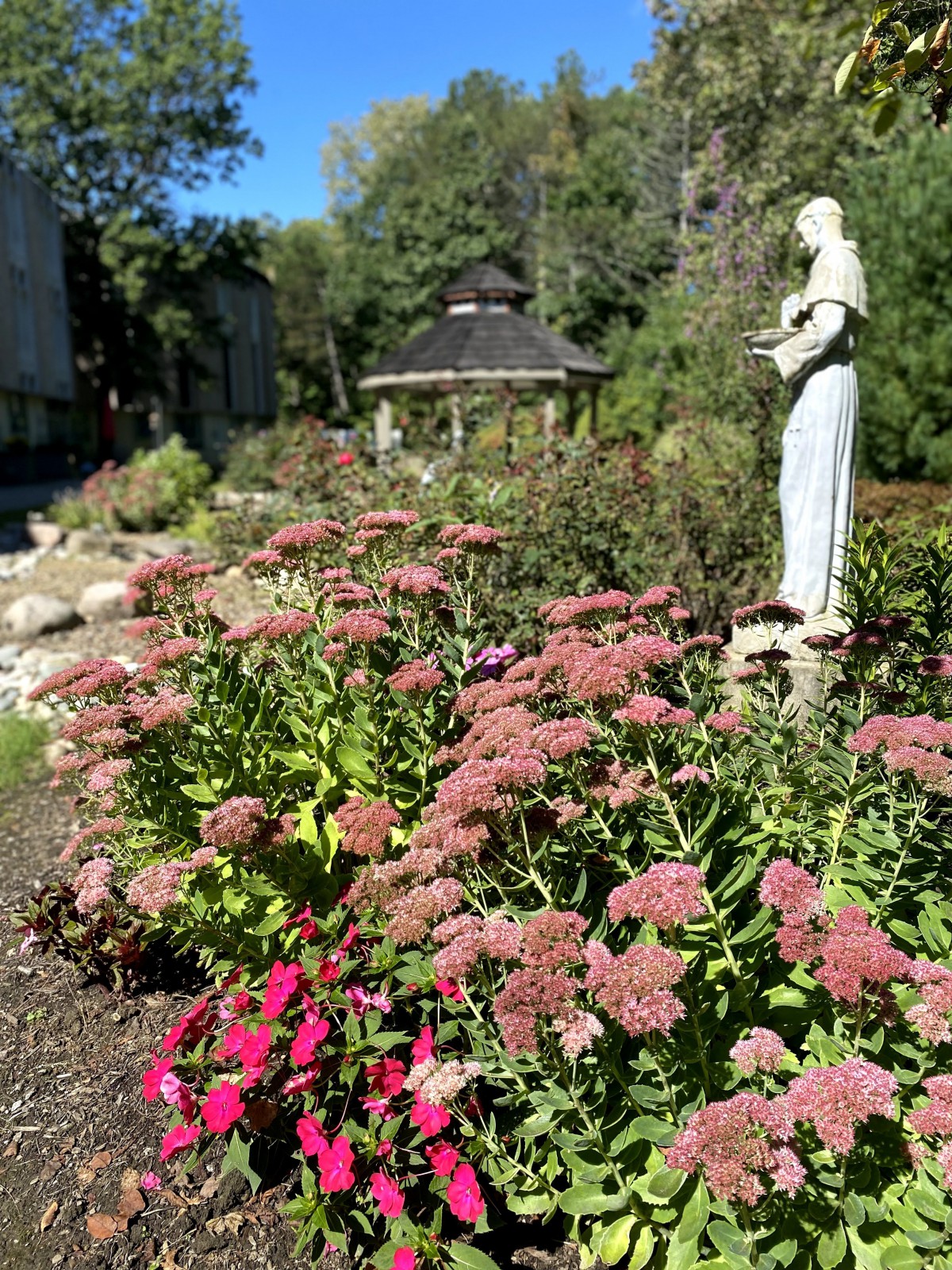 A serene garden with a statue, vibrant flowers, and a gazebo in the background.