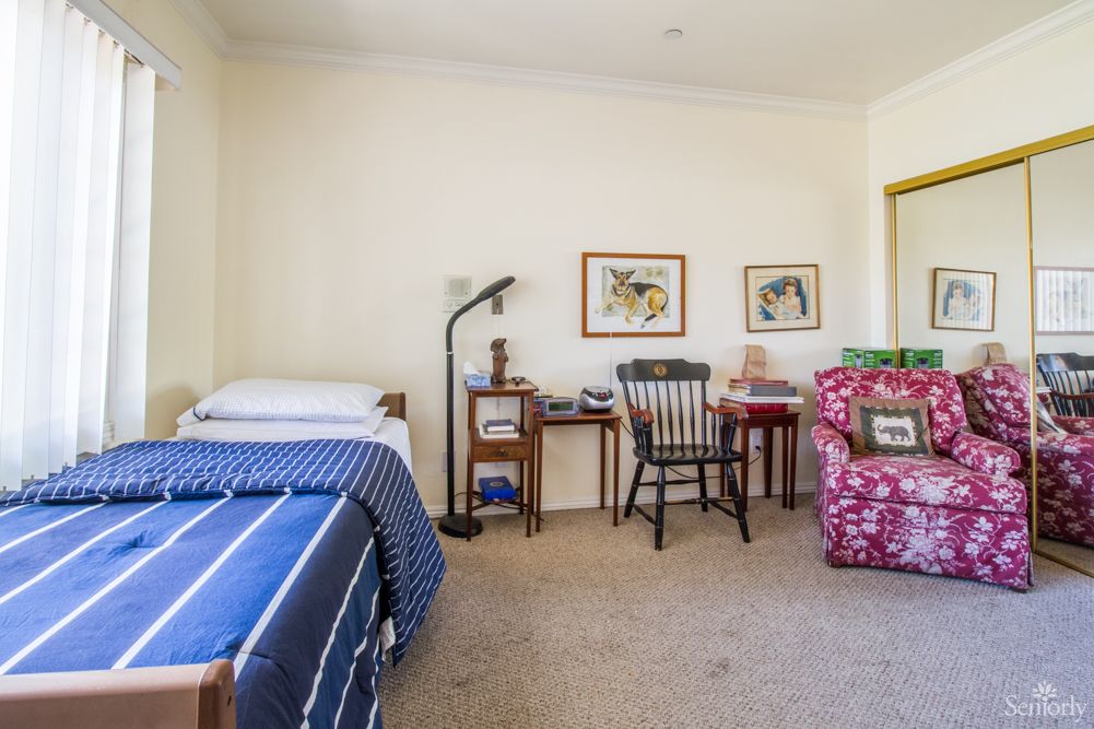 A cozy bedroom with a bed, desk, chair, and vibrant armchair.