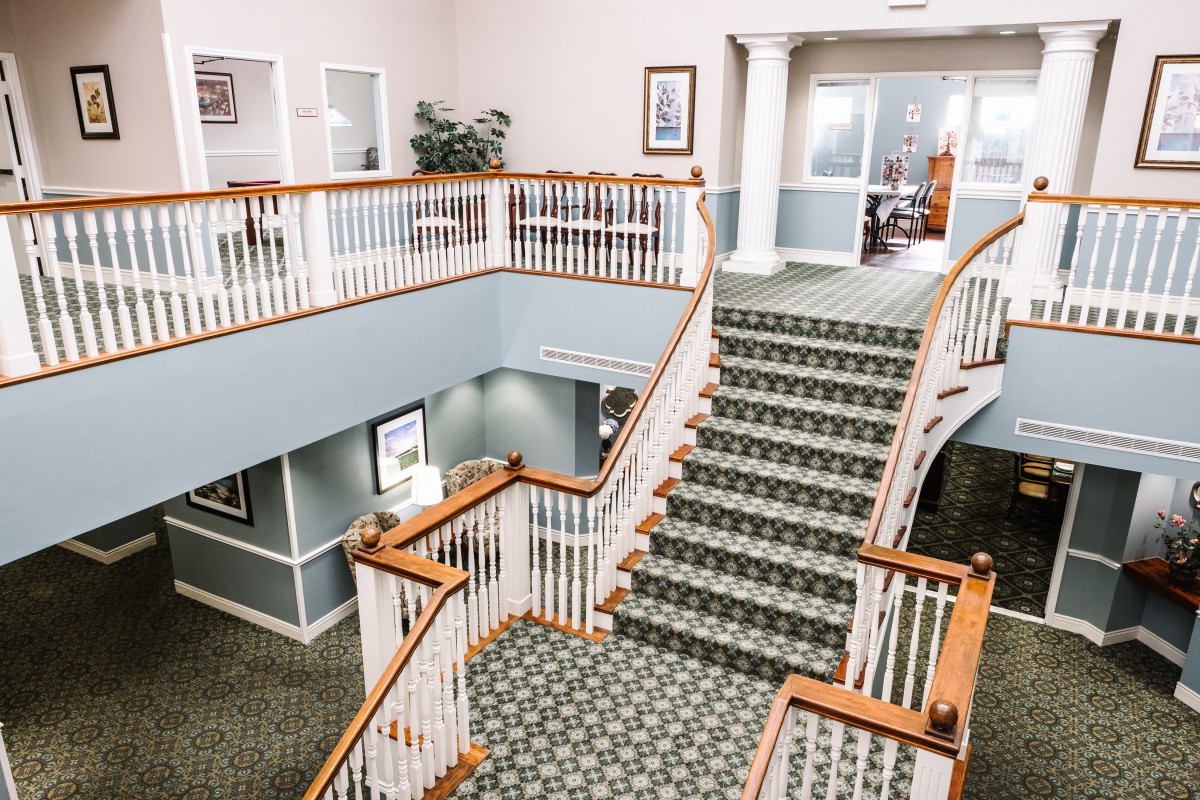 A spacious building interior featuring a grand staircase with carpet and wooden banisters.