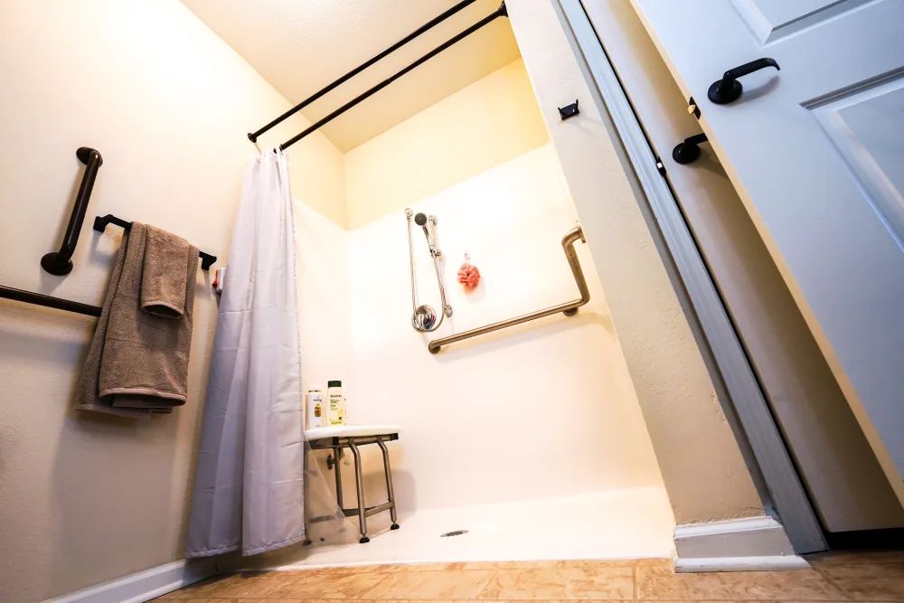 An accessible bathroom with a shower featuring grab bars and a bench.