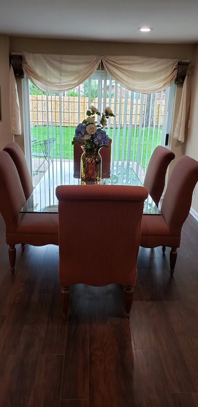 A dining area featuring a glass-top table and four upholstered chairs, adorned with a decorative vase and flowers.