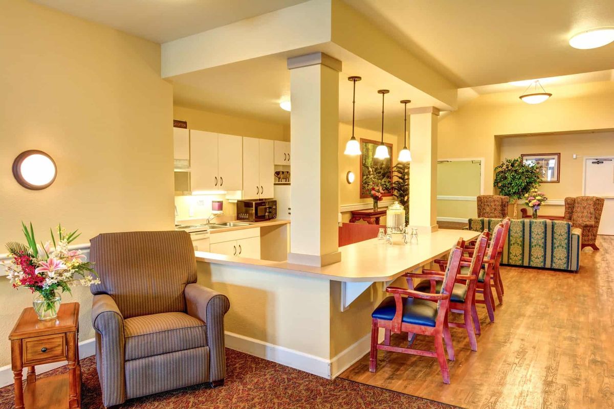 A modern open-concept kitchen and living area featuring a long counter with bar stools, warm lighting, and cozy seating.