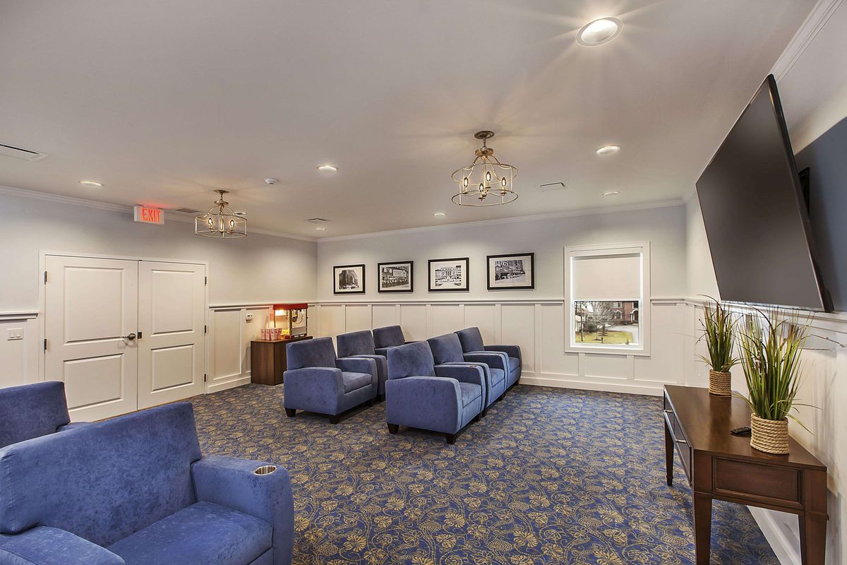 A cozy living room with blue chairs, chandeliers, and framed pictures on the wall.