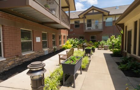 A sunny courtyard featuring benches and lush greenery in a residential building setting.