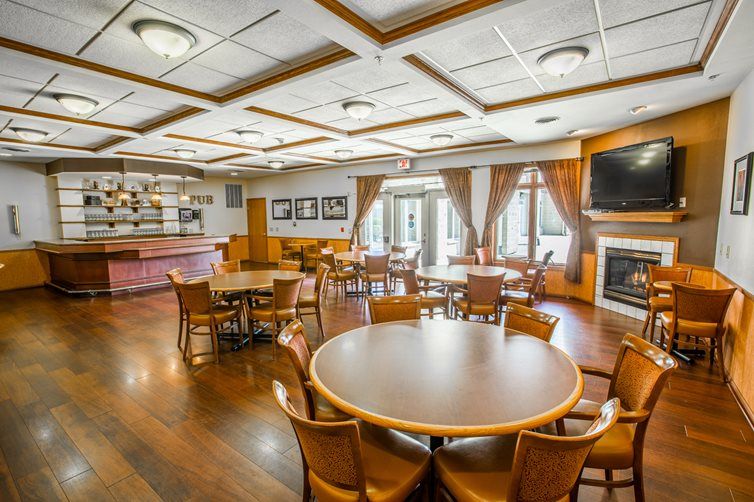 A spacious dining area with round tables, wooden flooring, and warm lighting, creating a cozy atmosphere.