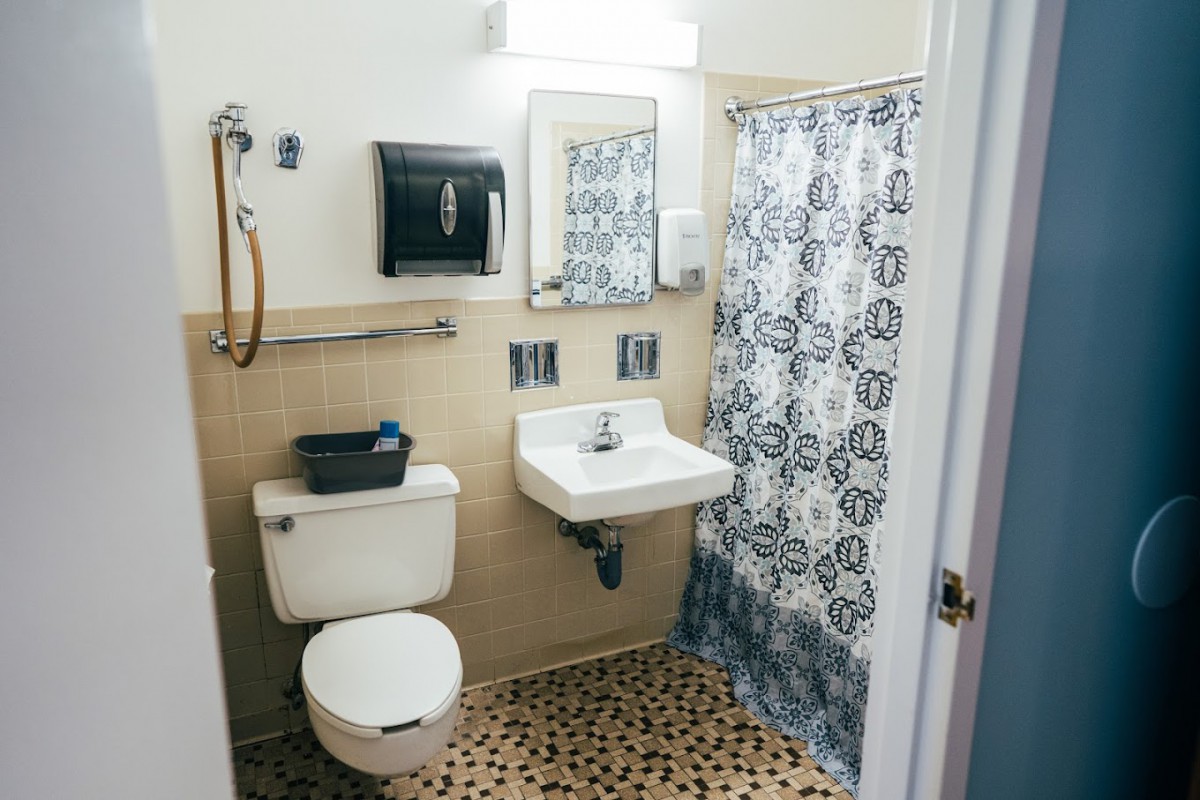 A small bathroom with a toilet, sink, and shower, featuring a patterned shower curtain and tiled floor.