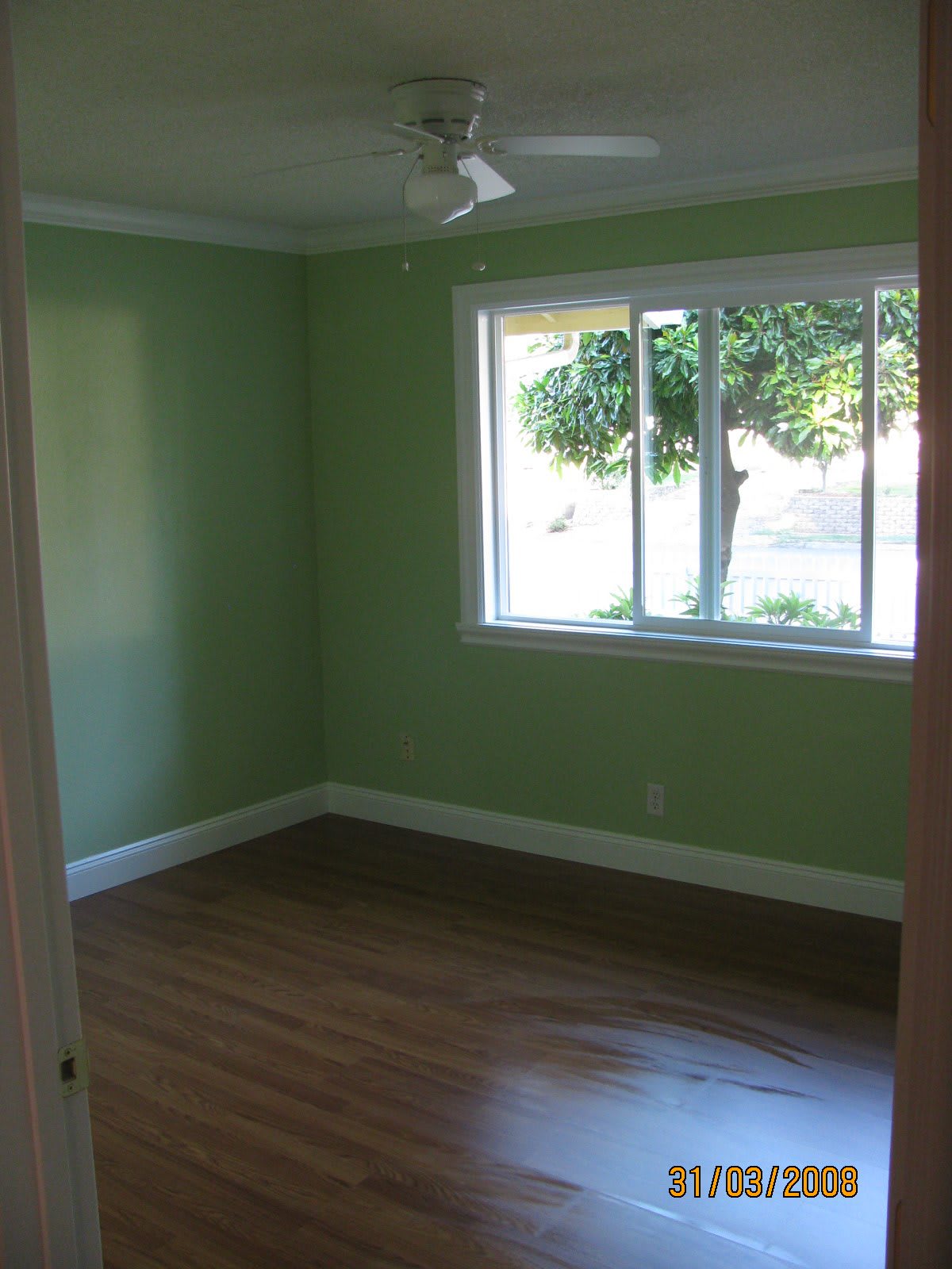 A view of an empty room with green walls, a large window, and wooden flooring.