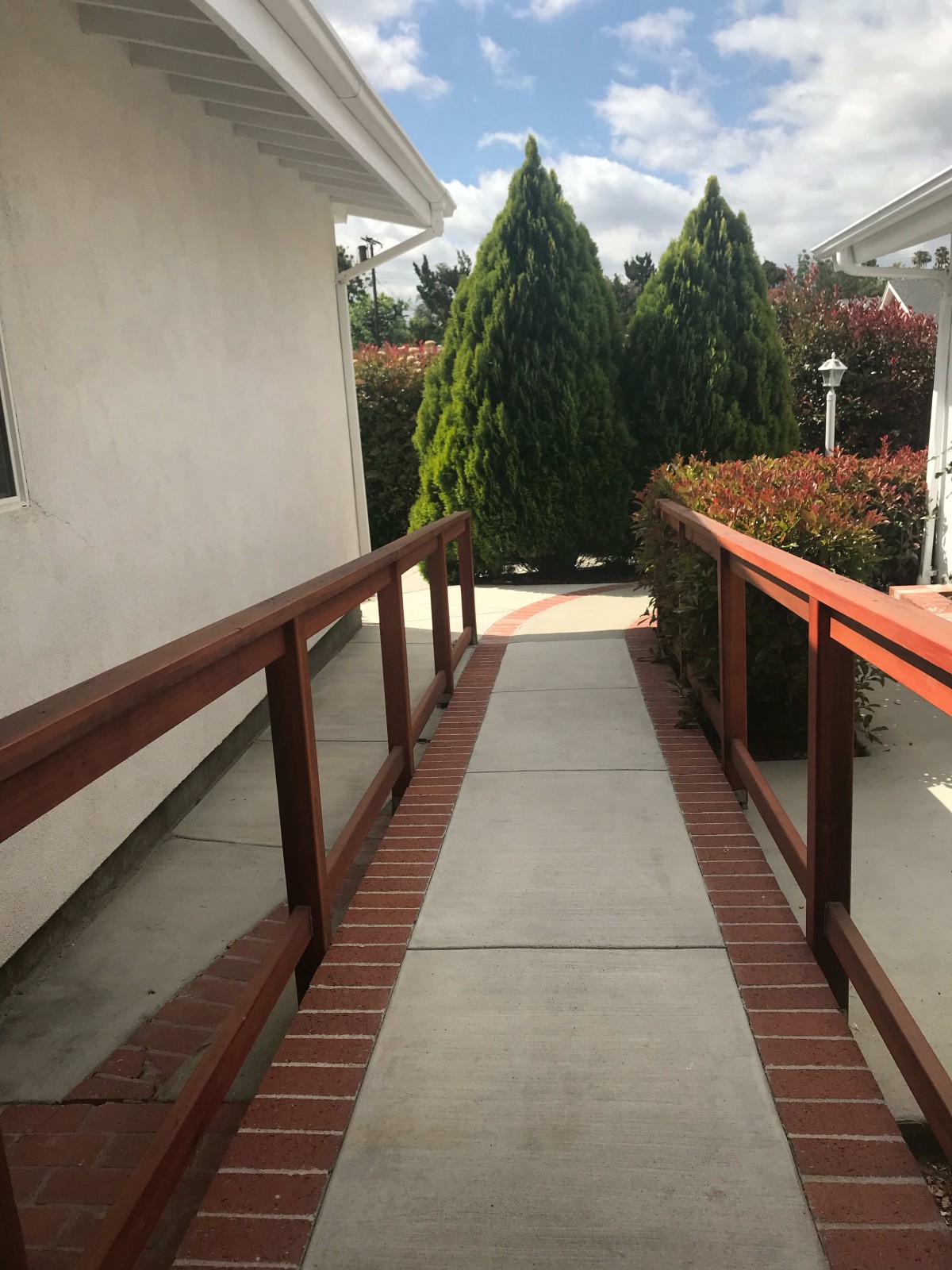 An outdoor ramp with wooden handrails leading through a garden area.