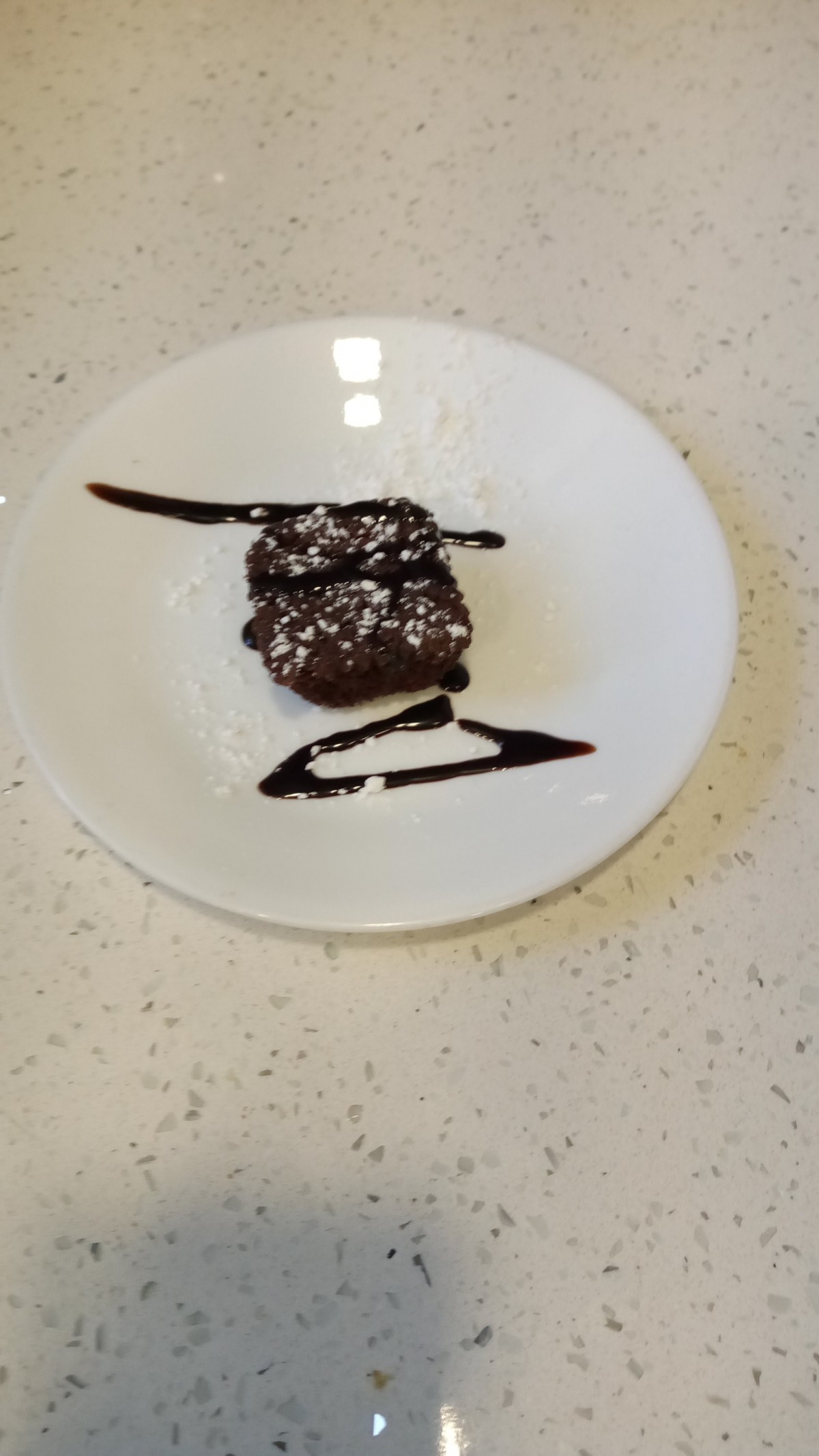 A beautifully plated chocolate brownie garnished with powdered sugar and chocolate drizzle.