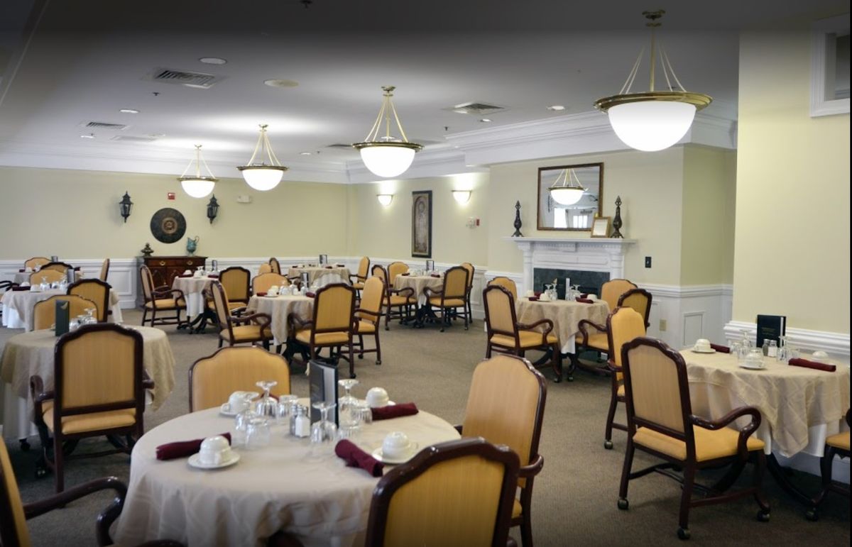 An elegant dining room with neatly arranged tables and chairs, featuring chandeliers and a fireplace.
