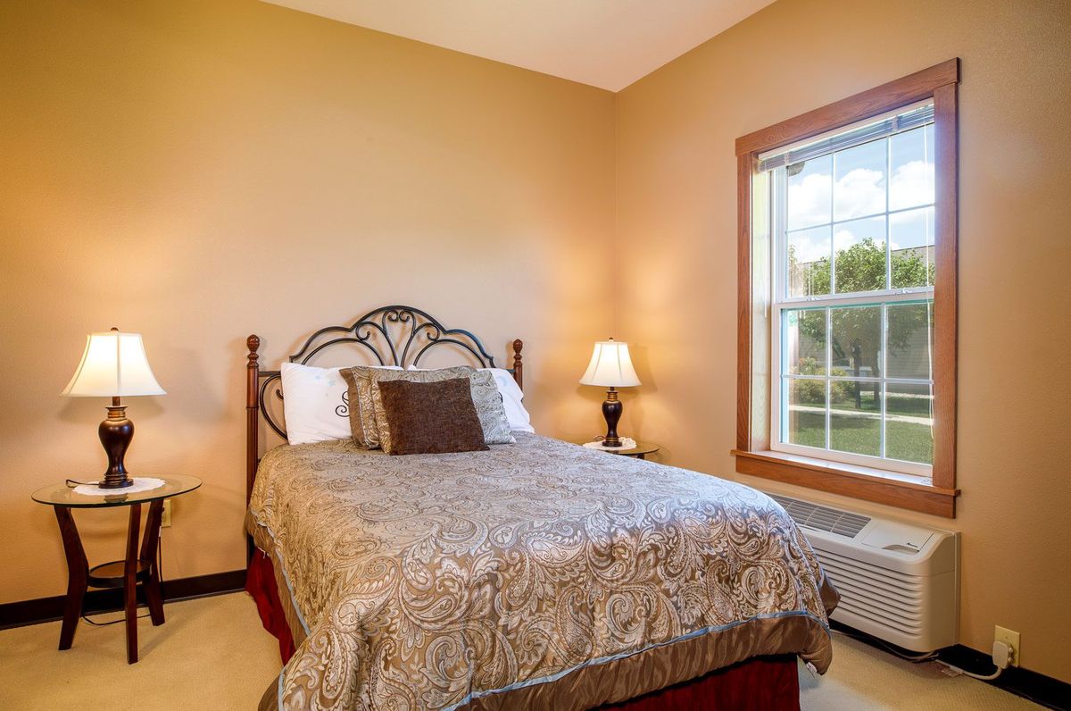 A cozy bedroom with a double bed, decorative pillows, and a bedside lamp next to a large window.
