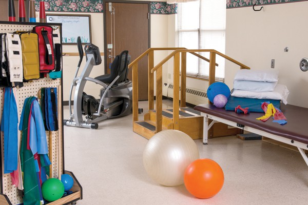 A rehabilitation room equipped with an exercise bike, therapy balls, and parallel bars designed for physical therapy exercises.