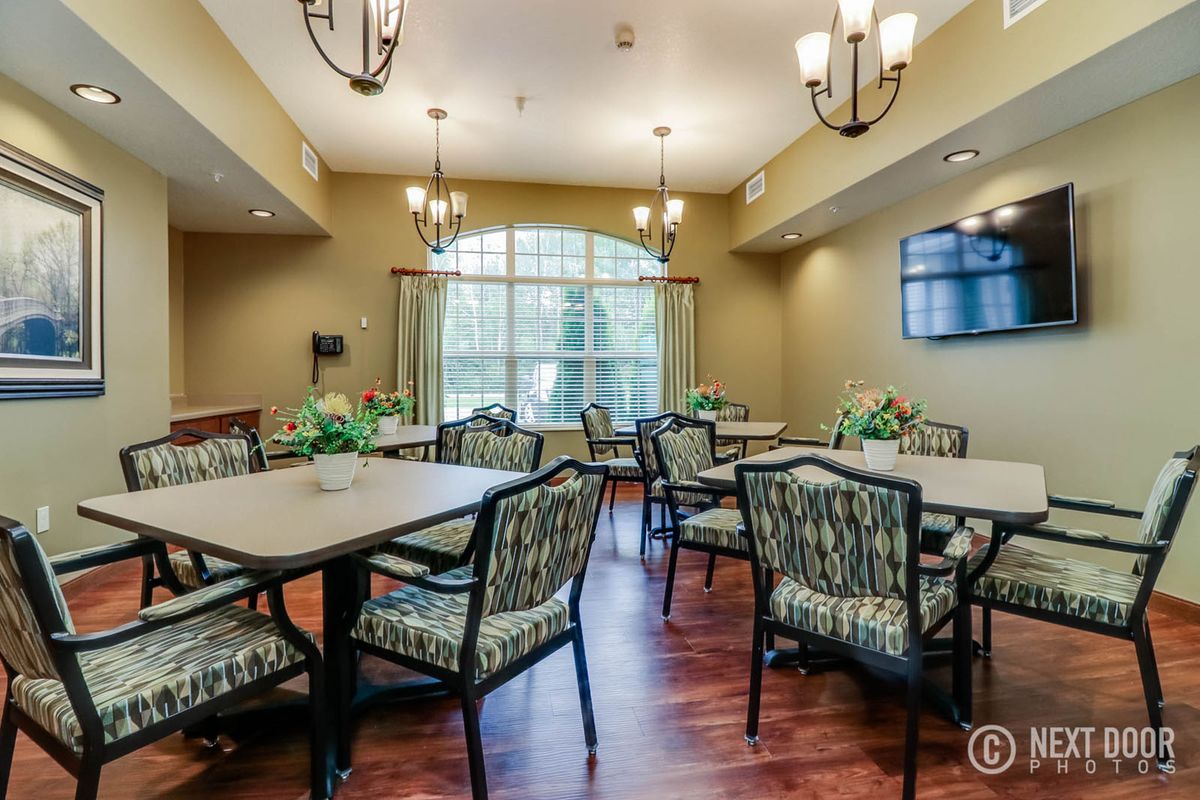 A well-lit dining room with multiple tables and chairs, featuring elegant chandeliers and a large window.