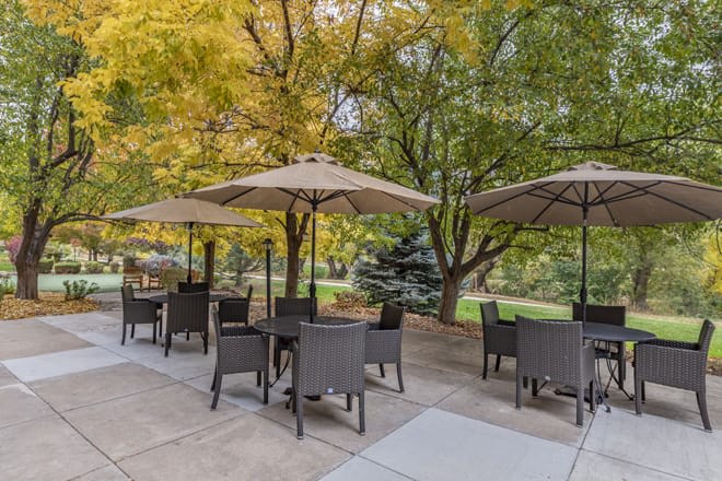 Outdoor patio area with tables, chairs, and umbrellas under autumn trees.