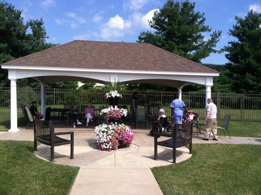 A gazebo in a garden setting with people enjoying the sunny day.
