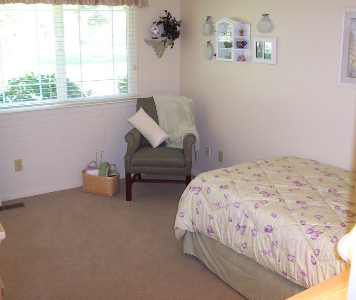 A cozy bedroom with a bed, an armchair, and a window letting in natural light.