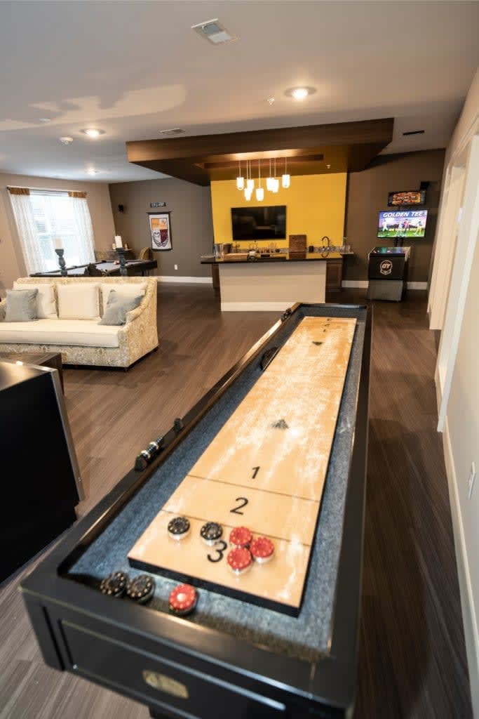 A modern game room featuring a shuffleboard table, bar area, and cozy seating.