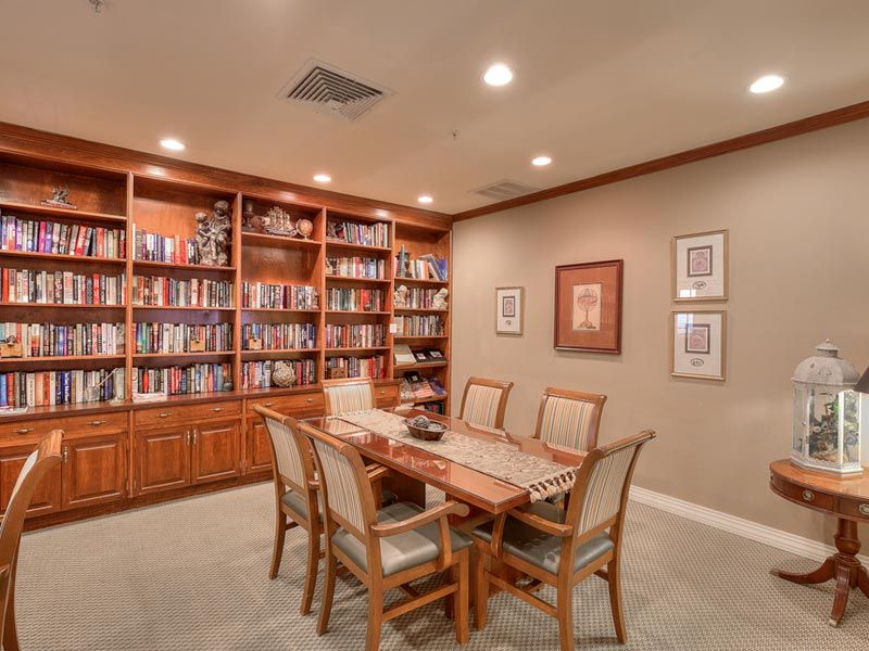 A cozy library room with wooden bookshelves filled with books, a large table, and chairs arranged neatly on a carpeted floor.