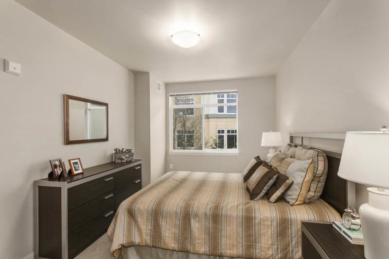 A neatly decorated bedroom with a bed, dresser, and window view.