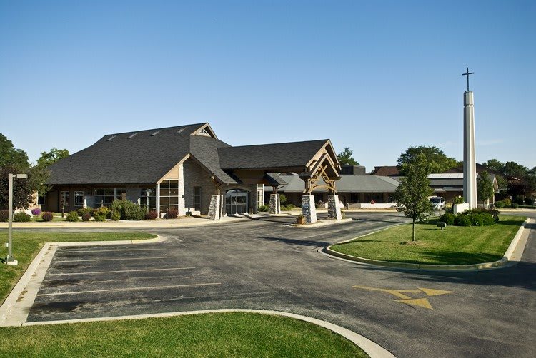 A modern building with a large parking area and landscaped surroundings under a clear blue sky.