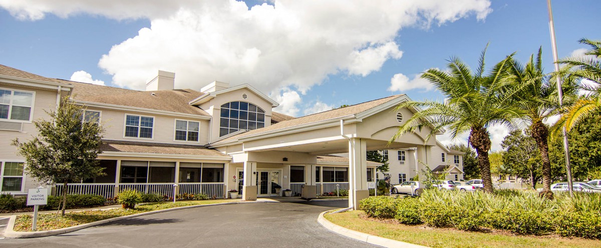 A modern building with a covered entrance and driveway under a partly cloudy sky.