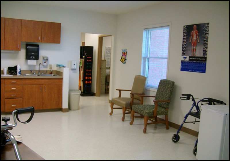 A medical waiting room with chairs, a walker, and informational posters on the walls.