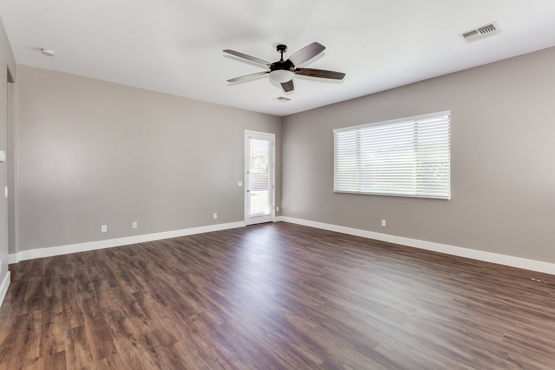 An empty living room with hardwood flooring and a ceiling fan.