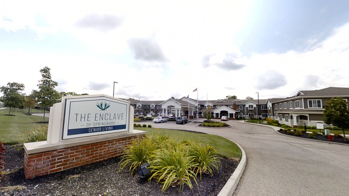 Entrance of a large building complex with a sign and landscaped driveway.