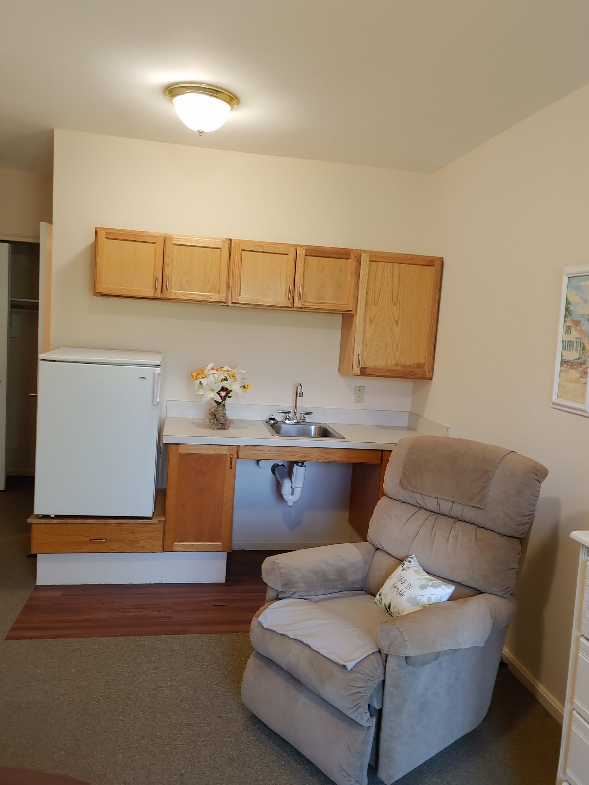 A cozy kitchenette area with a recliner, cabinets, and small appliances.