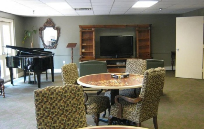 A cozy living room setup with patterned chairs around a table, a television, and a piano.
