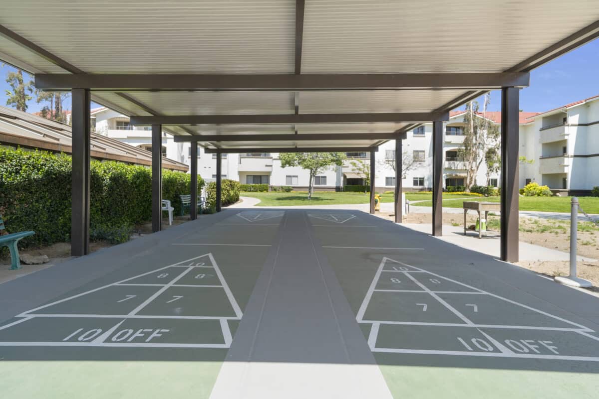 A covered outdoor shuffleboard court surrounded by greenery.