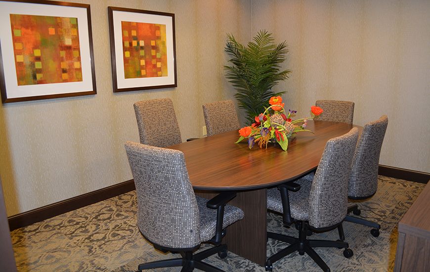 A neatly arranged conference room with a wooden meeting table surrounded by chairs, featuring decorative wall art and a potted plant.