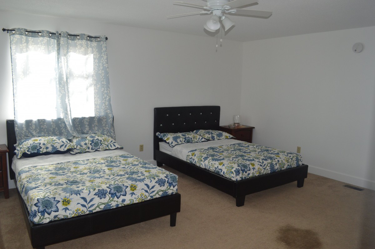 A simple bedroom with two twin beds and a window, featuring minimalist decor.